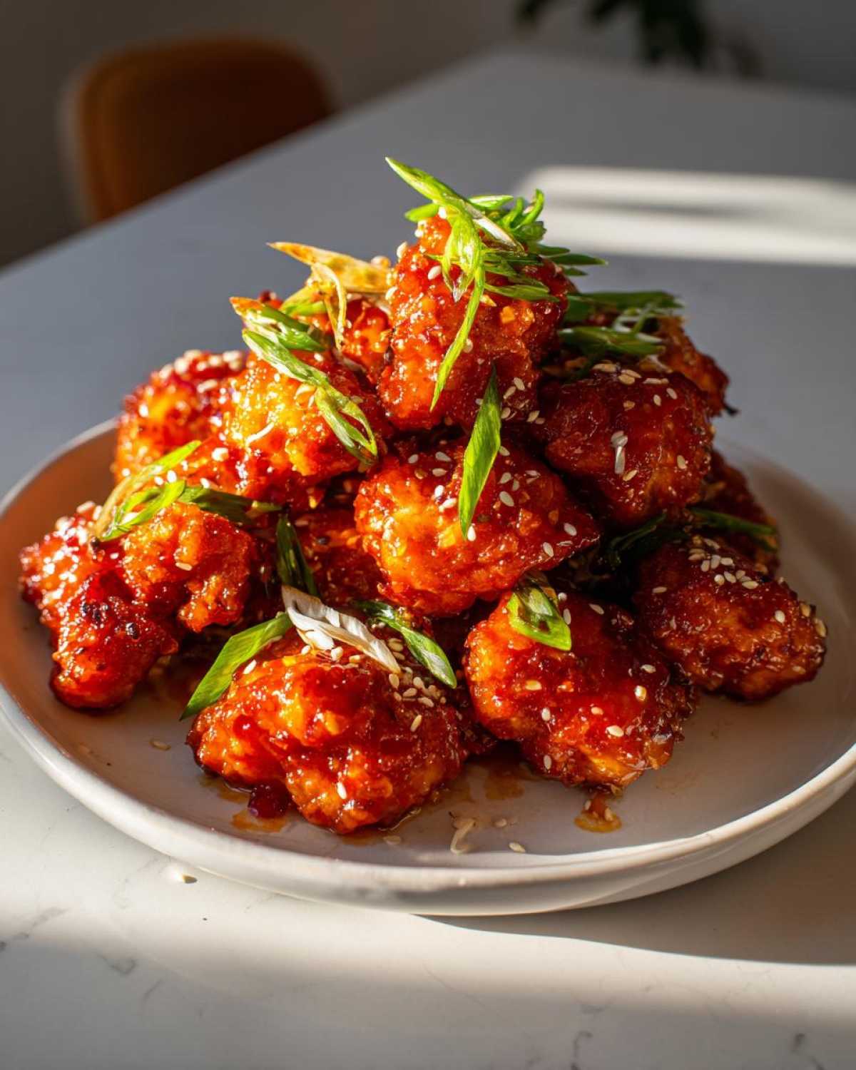A mound of glossy, red-glazed Air Fryer Crispy Korean Chicken Bites garnished with sesame seeds and sliced green onions.