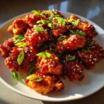 A close-up of Air Fryer Crispy Korean Chicken Bites coated in a glossy red sauce, sprinkled with sesame seeds and green onions.