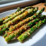 Close-up of bright green Air Fryer Crispy Parmesan Asparagus Fries arranged on a white plate.