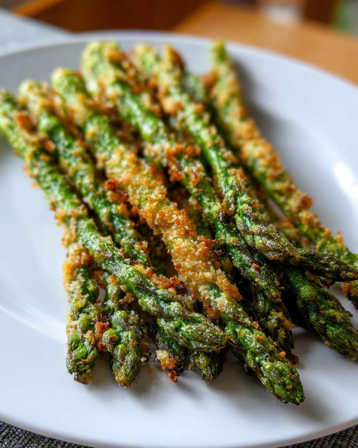 Close-up of perfectly cooked Air Fryer Crispy Parmesan Asparagus Fries piled on a white plate.