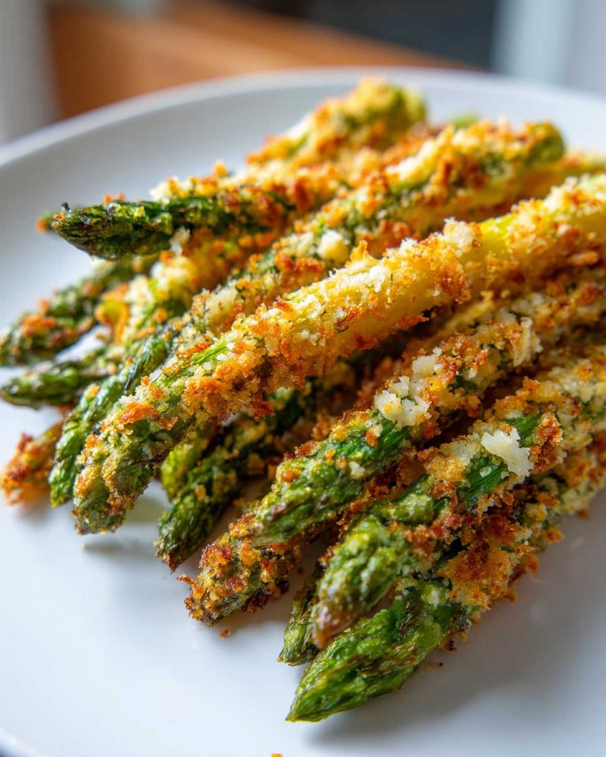 Close-up of perfectly cooked Air Fryer Crispy Parmesan Asparagus Fries piled on a white plate.