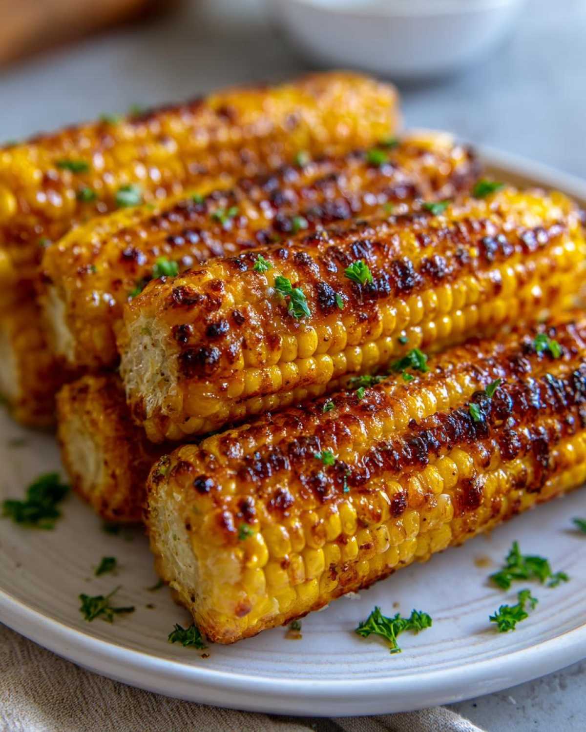 Close-up of several charred Air Fryer Crispy Parmesan Garlic Corn Ribs stacked on a white plate, garnished with parsley.
