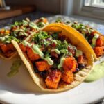 Close-up of several Air Fryer Crispy Sweet Potato Tacos topped with green sauce and cilantro on a white plate.