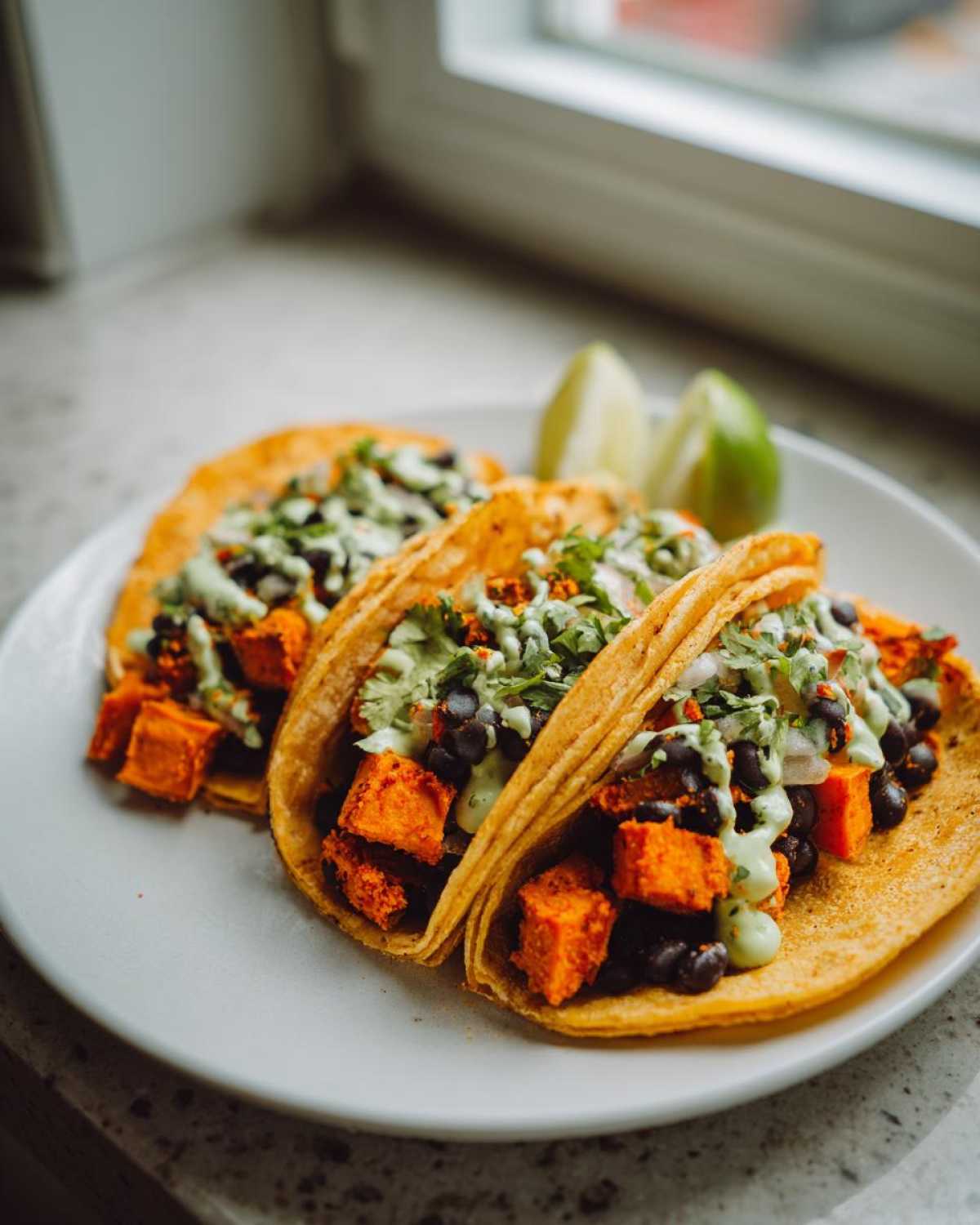 Three Air Fryer Crispy Sweet Potato Tacos filled with orange sweet potato cubes, black beans, and topped with green sauce and cilantro.