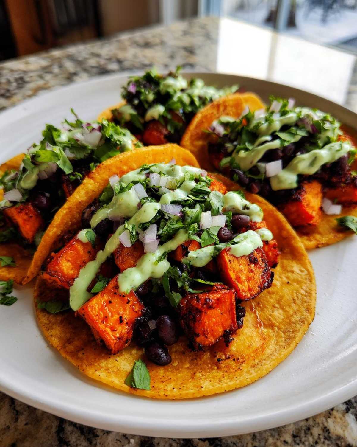 Close-up of Air Fryer Crispy Sweet Potato Tacos filled with seasoned sweet potato chunks, black beans, and topped with cilantro and avocado crema.