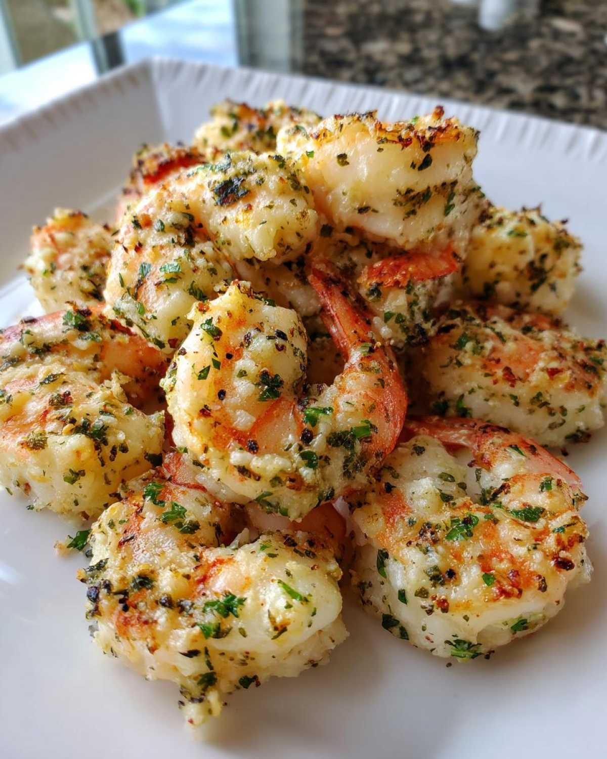 Close-up of juicy Air Fryer Garlic Parmesan Shrimp piled high on a white plate, coated in herbs.