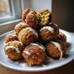 A stack of golden brown Air Fryer Herb Falafel Balls drizzled generously with white tahini sauce.