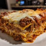 A thick, layered slice of baked lasagna with rich meat sauce and melted cheese topping.