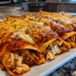 Close-up of freshly baked chicken enchiladas covered in red sauce and melted cheese, revealing shredded chicken filling.