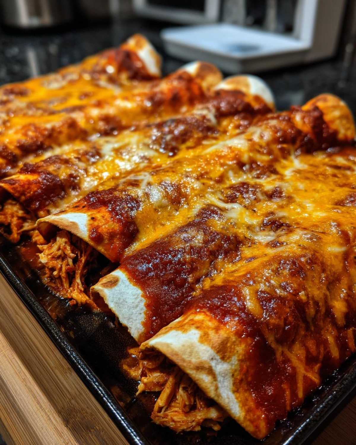 Close-up of baked enchiladas covered in rich red sauce and melted orange cheese, showing shredded chicken filling.
