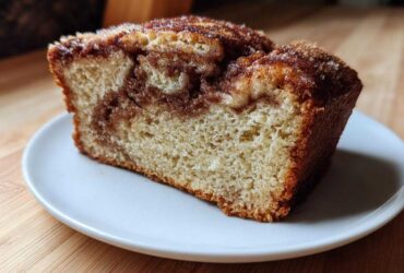 Close-up of a moist slice of Amish Cinnamon Bread showing a rich cinnamon swirl and sugary top.