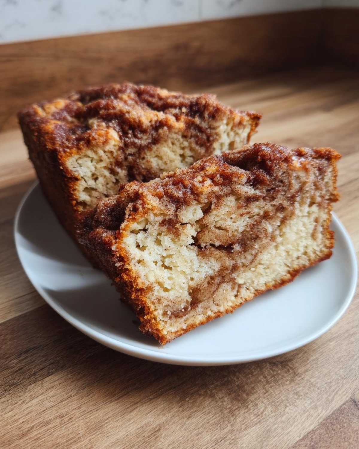 Two thick slices of moist Amish Cinnamon Bread with a visible cinnamon swirl topping on a white plate.