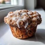 A single, perfectly baked Apple Fritter Muffins With a Glaze, topped with cinnamon streusel and dripping white icing.