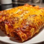 Close-up of three baked enchiladas covered in bubbling, melted cheddar cheese, perfect for an Enchiladas Dinner.