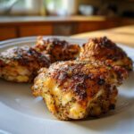 Four golden-brown Baked Ranch Chicken Thighs seasoned heavily with herbs, served on a white plate.