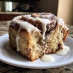 Close-up of a single, moist Banana Bread Batter Cinnamon Buns slice covered in thick white icing.