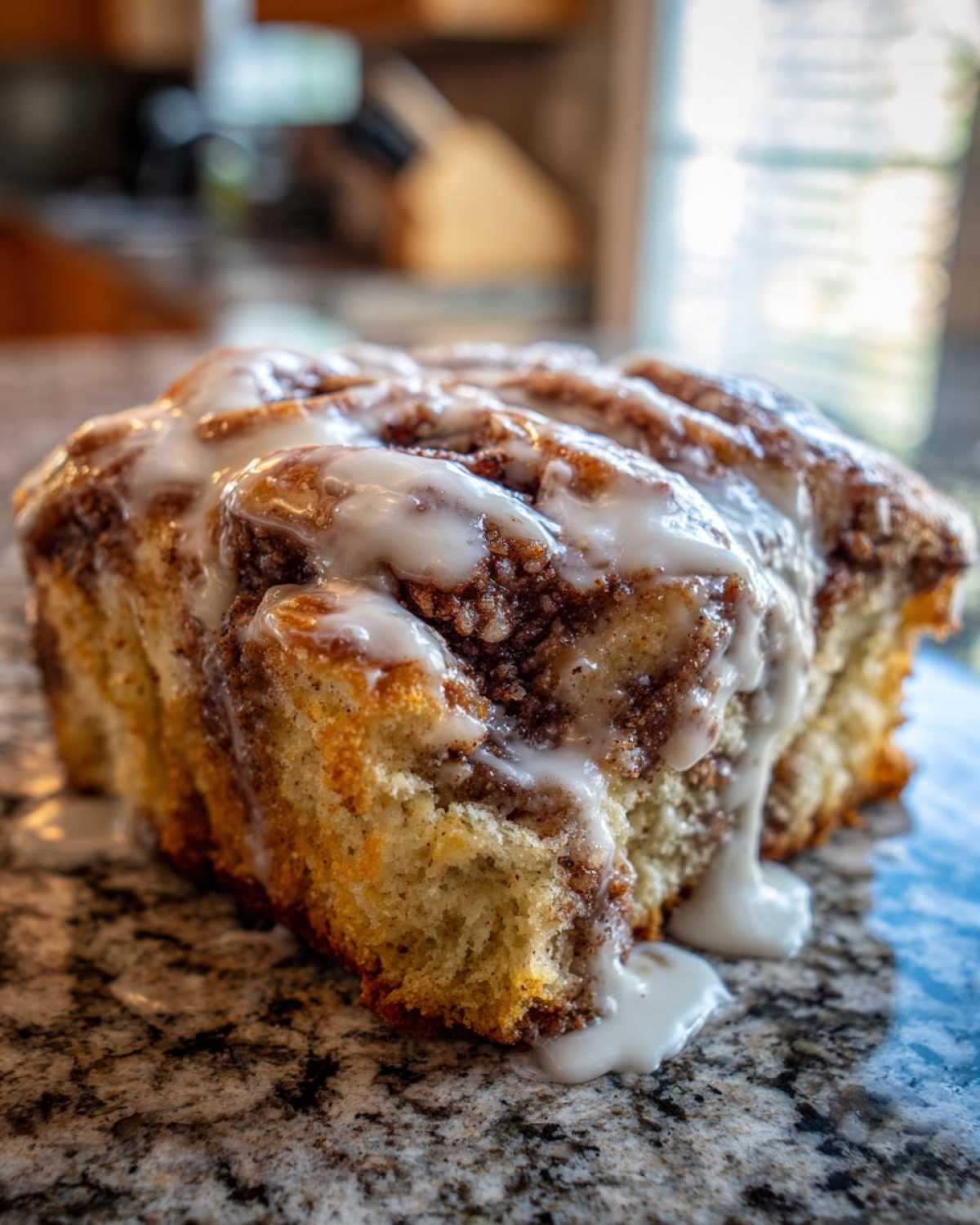 A close-up of a soft, glazed portion of Banana Bread Batter Cinnamon Buns drizzled with white icing.