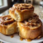 A stack of gooey Biscoff Cookie Butter Cinnamon Rolls drizzled with caramel icing on a white plate.