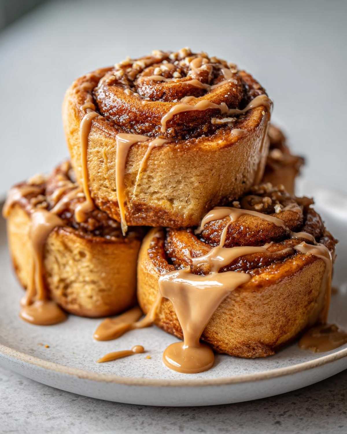 A stack of three decadent Biscoff Cookie Butter Cinnamon Rolls drizzled heavily with Biscoff glaze and topped with nuts.
