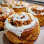 A close-up, tempting shot of one of the Carrot Cake Cinnamon Rolls with Creamy Frosting, topped with shredded carrots.