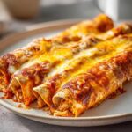 Close-up of three baked enchiladas covered in red sauce and melted golden cheese, perfect for an Enchiladas Dinner.