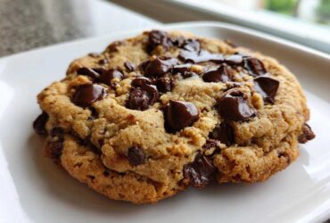 Close-up of a gooey, freshly baked Chocolate Chip Cookie For One with melted chocolate chunks on a white plate.