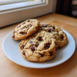 Three perfectly baked Chocolate Chip Cookies with Pudding Mix stacked slightly on a white plate.