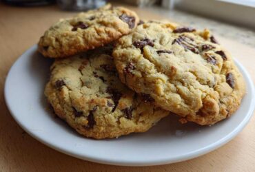Three freshly baked Chocolate Chip Cookies with Pudding Mix stacked slightly on a small white plate.
