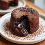 Close-up of a warm Chocolate Lava Cake with molten chocolate oozing out, dusted with cocoa powder.