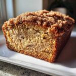 A close-up, cross-section view of a slice of Cinnamon Crumb Banana Bread with a thick, sugary cinnamon topping.