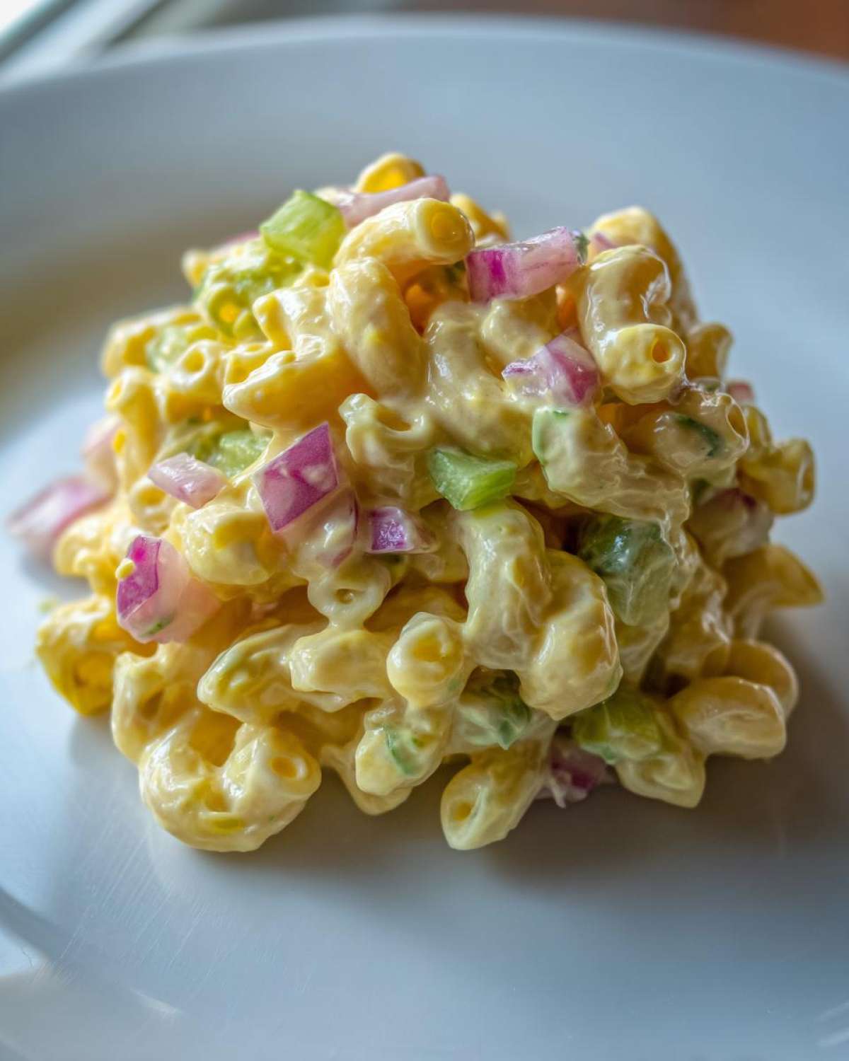Close-up of a scoop of Classic Macaroni Salad Creamy Summer Side mixed with diced red onion and celery.