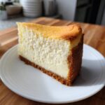 A perfect slice of Classic New York Cheesecake showing a thick, creamy filling and a rich graham cracker crust.