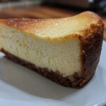 A perfect slice of Classic New York Cheesecake showing a creamy interior and dark graham cracker crust.