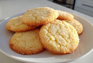 A stack of freshly baked Classic Vanilla Sugar Cookies, coated generously with sparkling granulated sugar, resting on a white plate.