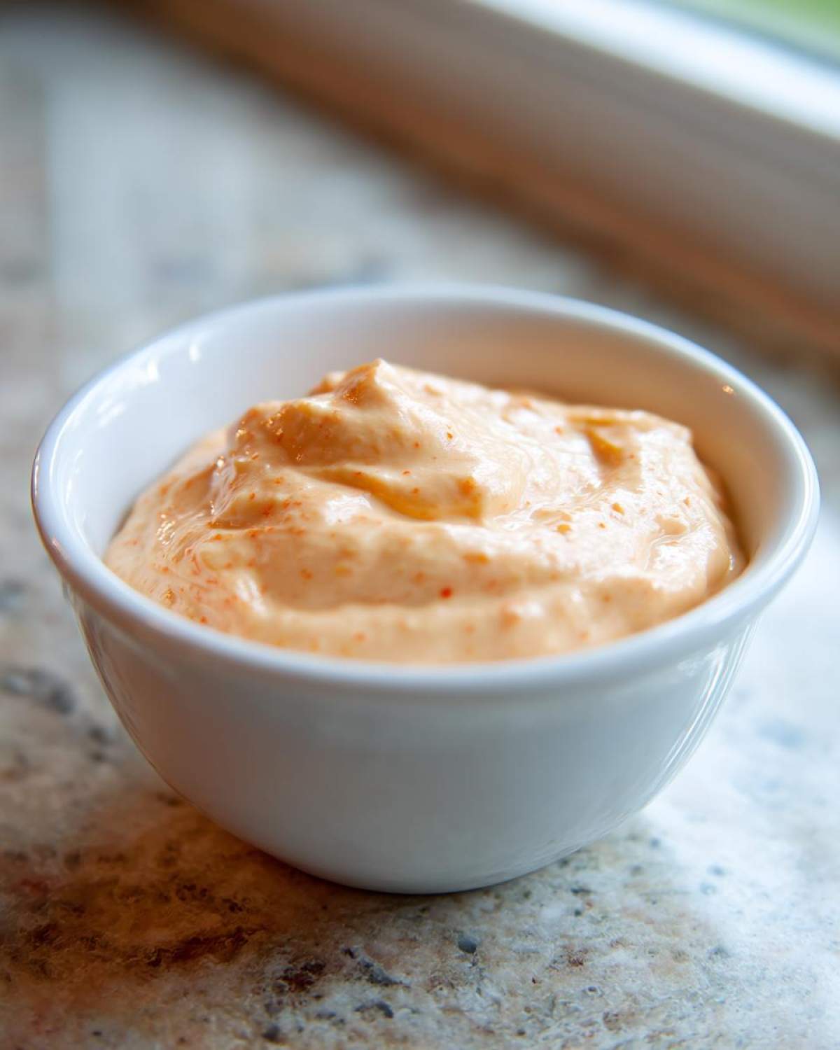 A close-up of creamy, orange-hued Copycat Classic Burger Spread Sauce served in a small white dipping bowl.