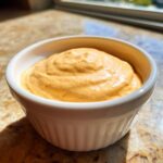 A close-up of thick, orange-hued Copycat Classic Burger Spread Sauce swirled in a small white ramekin.