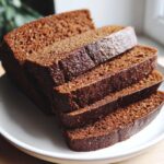 Four thick slices of rich, dark brown honey wheat bread stacked on a white plate.