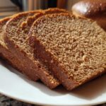 Close-up of four thick slices of Copycat Dark Brown Honey Wheat Bread arranged on a white plate.