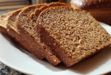 Close-up of four thick slices of Copycat Dark Brown Honey Wheat Bread arranged on a white plate.
