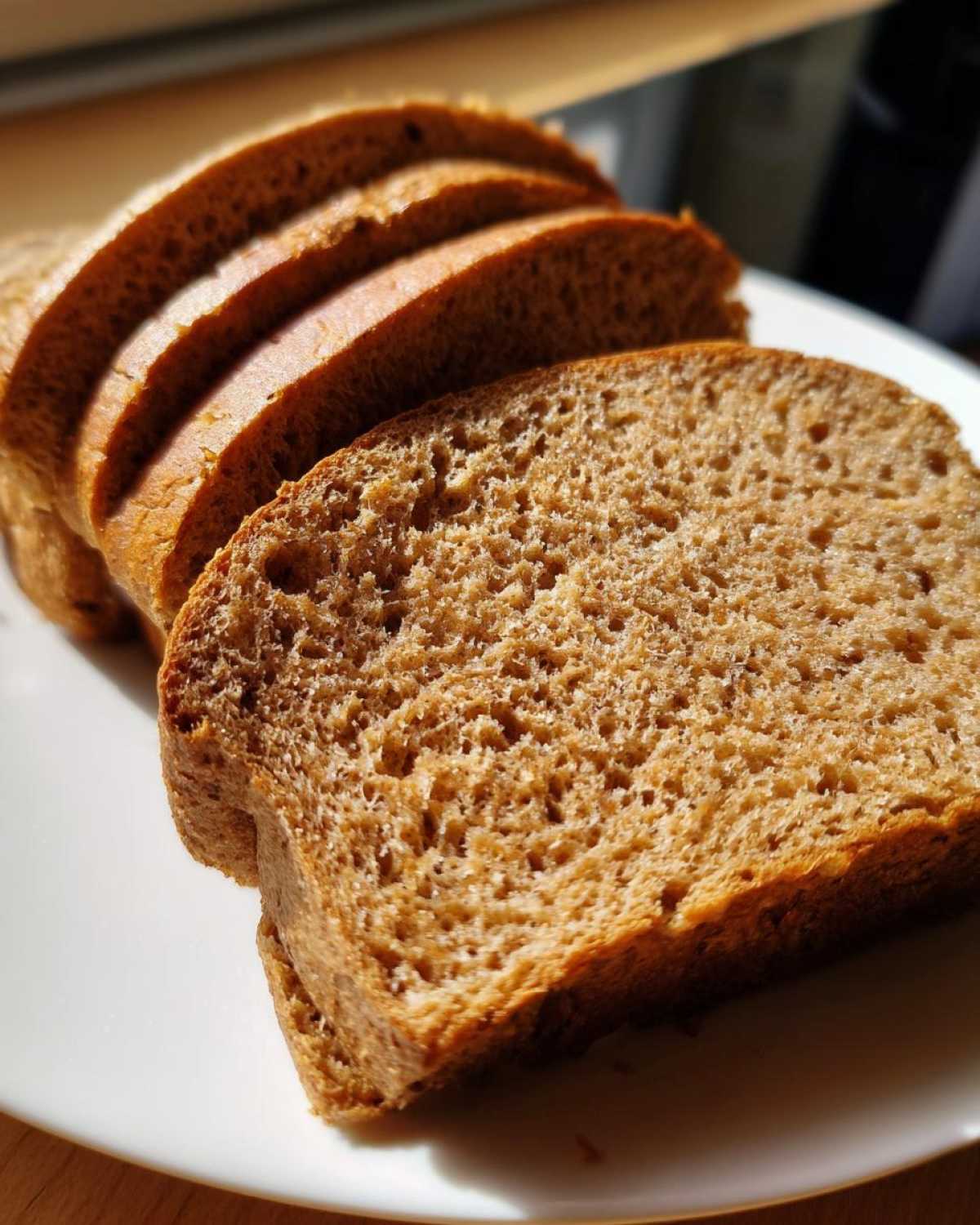 Close-up of four thick slices of Copycat Dark Brown Honey Wheat Bread stacked slightly on a white plate.