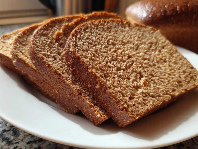 Close-up of four thick slices of Copycat Dark Brown Honey Wheat Bread arranged on a white plate.