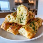 A stack of Copycat Italian Restaurant Soft Garlic Breadsticks, one piece pulled apart showing the soft, fluffy interior coated in garlic butter and parsley.