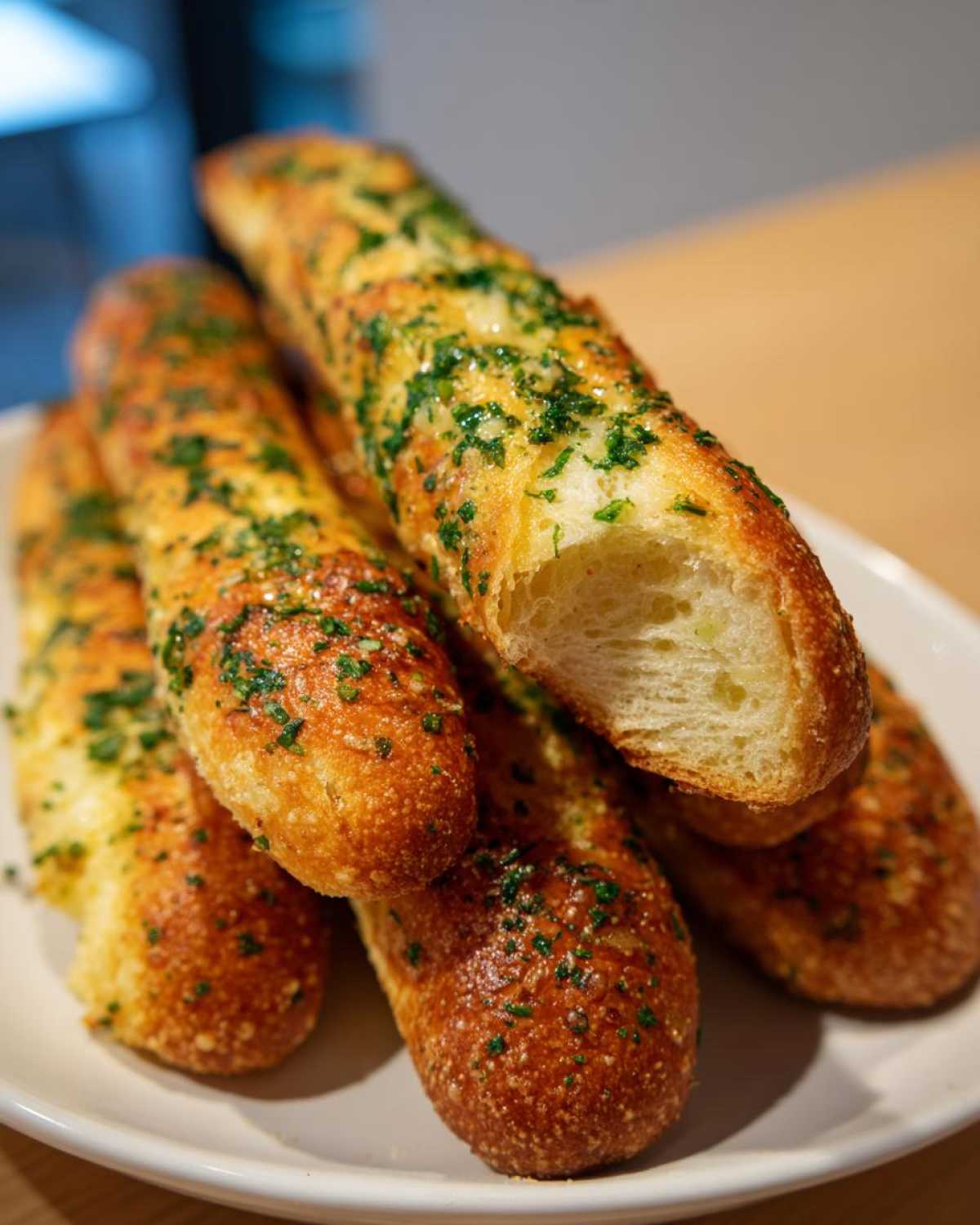A stack of golden brown Copycat Italian Restaurant Soft Garlic Breadsticks topped with melted butter and fresh green parsley.