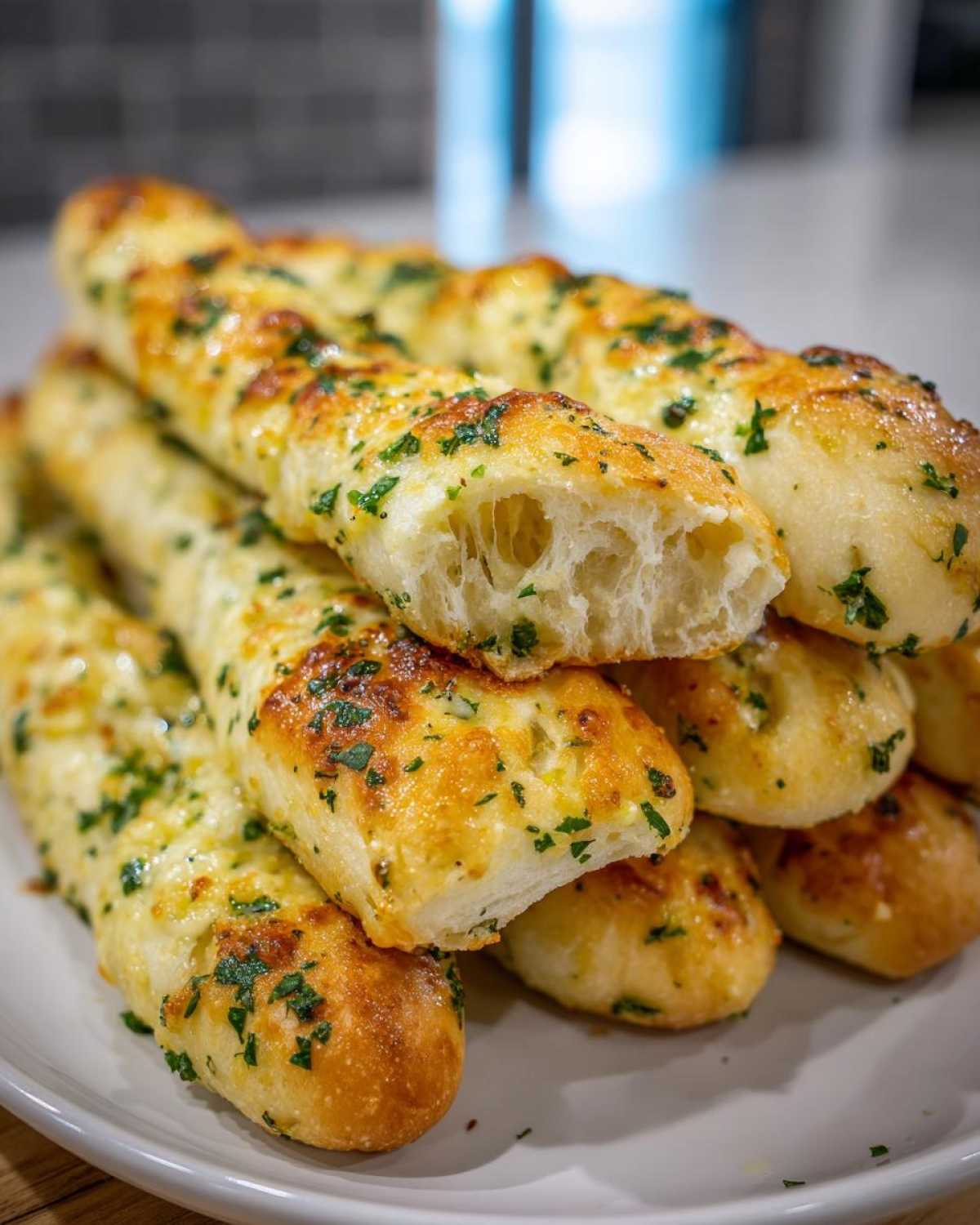 A stack of soft Copycat Italian Restaurant Soft Garlic Breadsticks topped with melted cheese and fresh parsley.