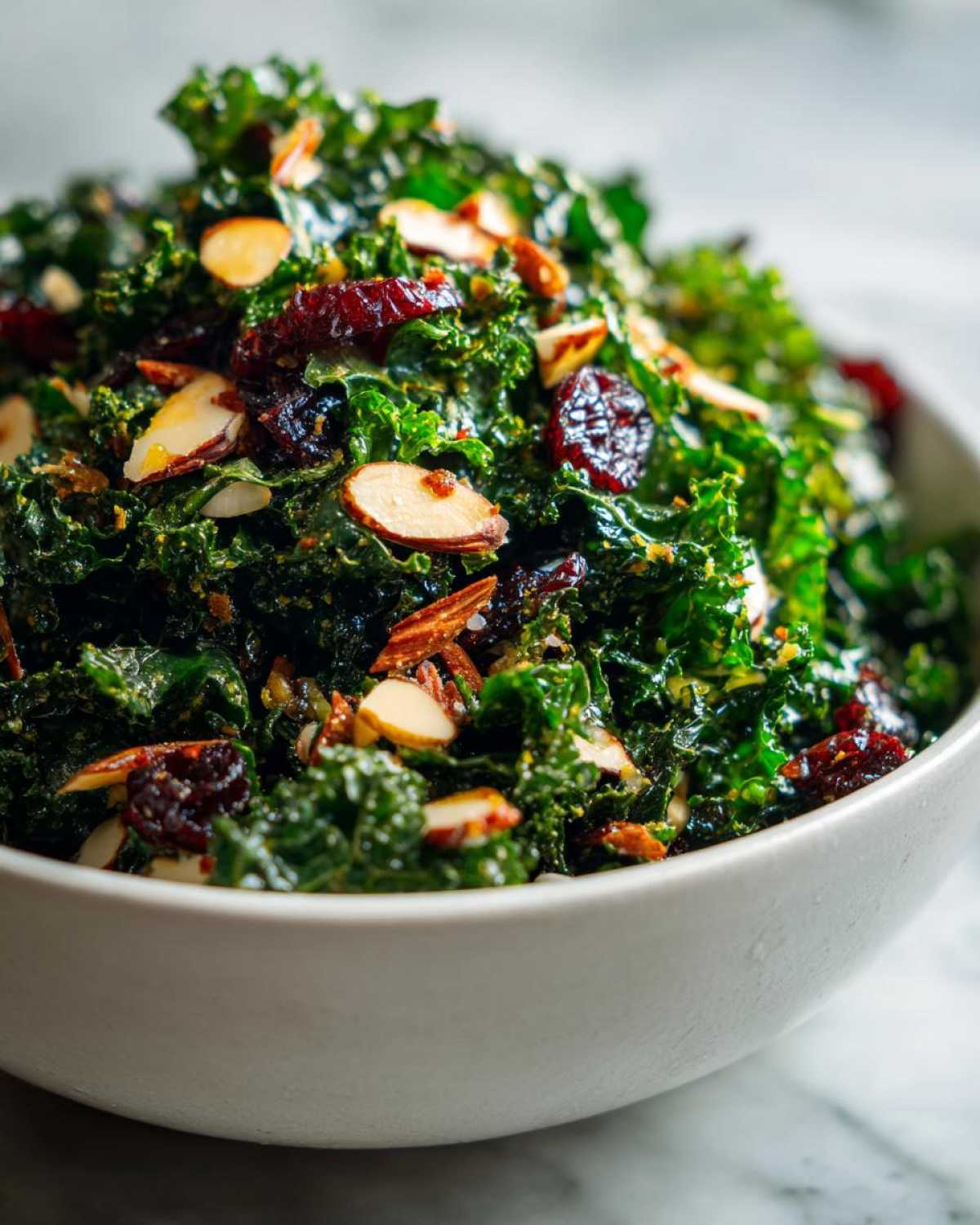 Close-up of a bowl filled with Copycat Kale Crunch Salad featuring vibrant green kale, sliced almonds, and dried cranberries.