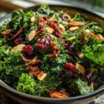 A close-up bowl of Copycat Kale Crunch Salad featuring bright green kale tossed in dressing, topped with dried cranberries, slivered almonds, and crispy bits.