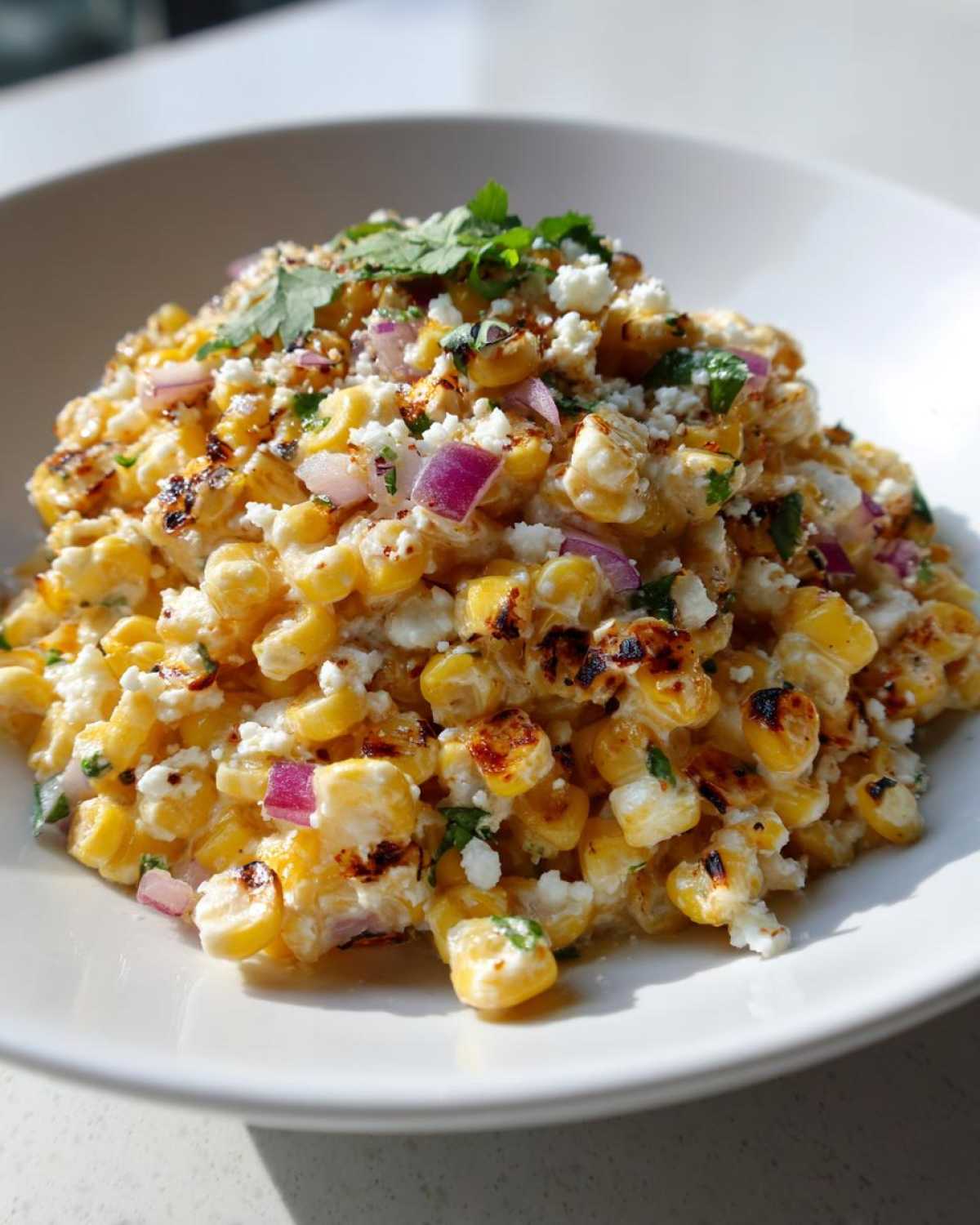 A close-up of creamy, charred corn kernels mixed with cotija cheese, red onion, and cilantro, representing Copycat Mexican Grill Corn Salsa.