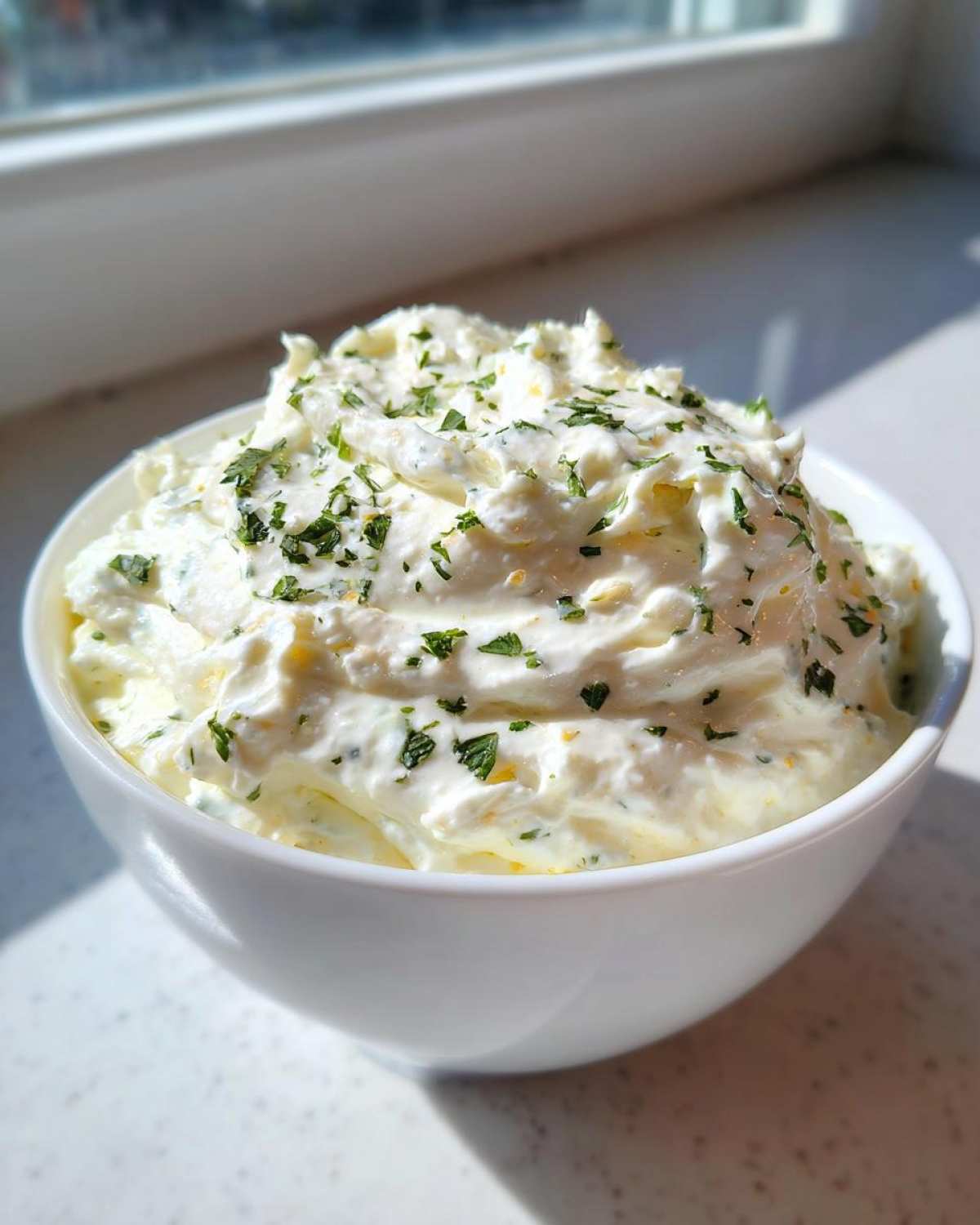A white bowl filled with creamy Copycat Pizza Garlic Parmesan Dip Sauce, topped with fresh parsley.