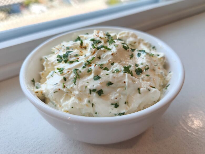 A close-up of thick, creamy Copycat Pizza Garlic Parmesan Dip Sauce garnished with fresh parsley in a small white bowl.