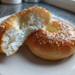 A close-up of a Cottage Cheese Bagels Breakfast, sliced in half to show the fluffy, white cottage cheese interior, topped with seeds.